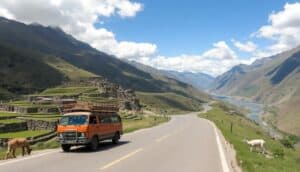 An orange van winds through Peru’s Sacred Valley, passing terraced hills and ancient stone ruins. Horses and goats graze nearby as a river cuts through the lush valley beneath a bright, partly cloudy sky—a perfect road trip scene.